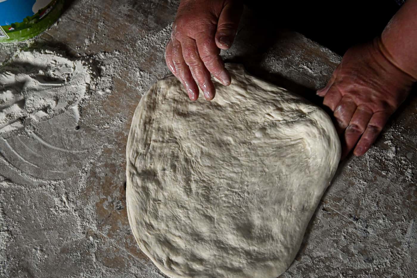 Hands stretching pizza dough on a floured counter